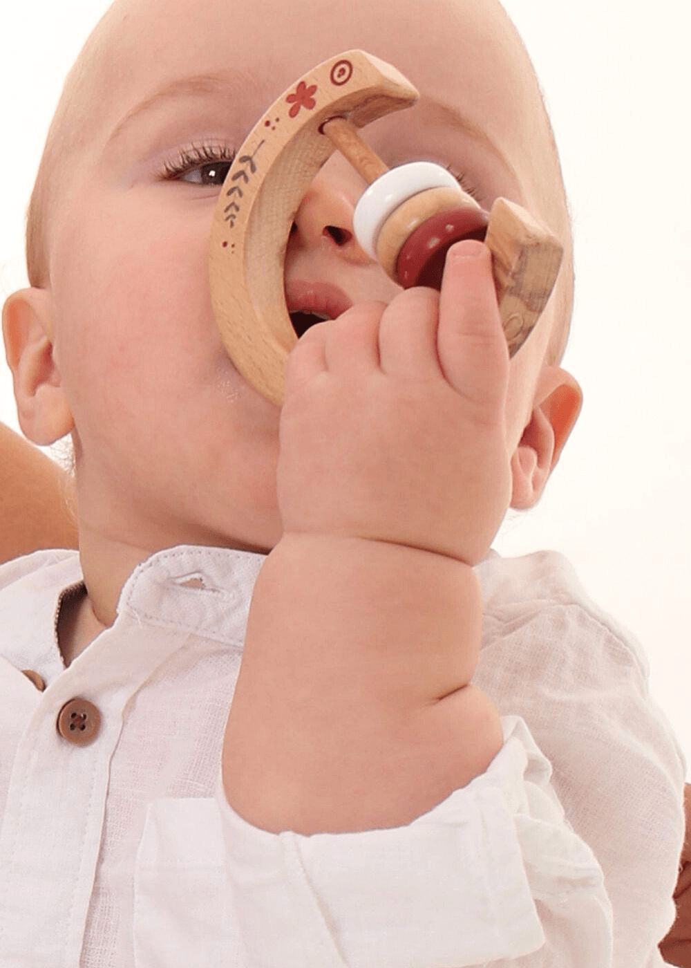 Baby holding a Wooden Baby Rattle from Bebe Pure, designed for grasping and teething with a curved wooden shape.