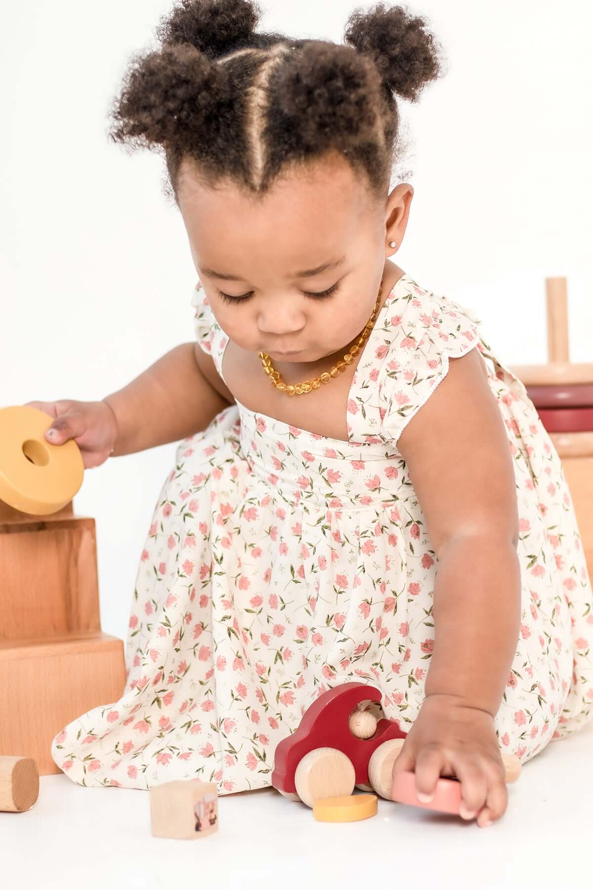 Toddler playing with wooden toys while wearing a floral dress from the Bebe Pure Collection.