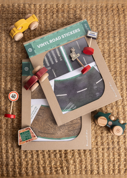 Wooden car, truck, and vinyl road stickers laid on a natural woven surface, perfect for creative play.