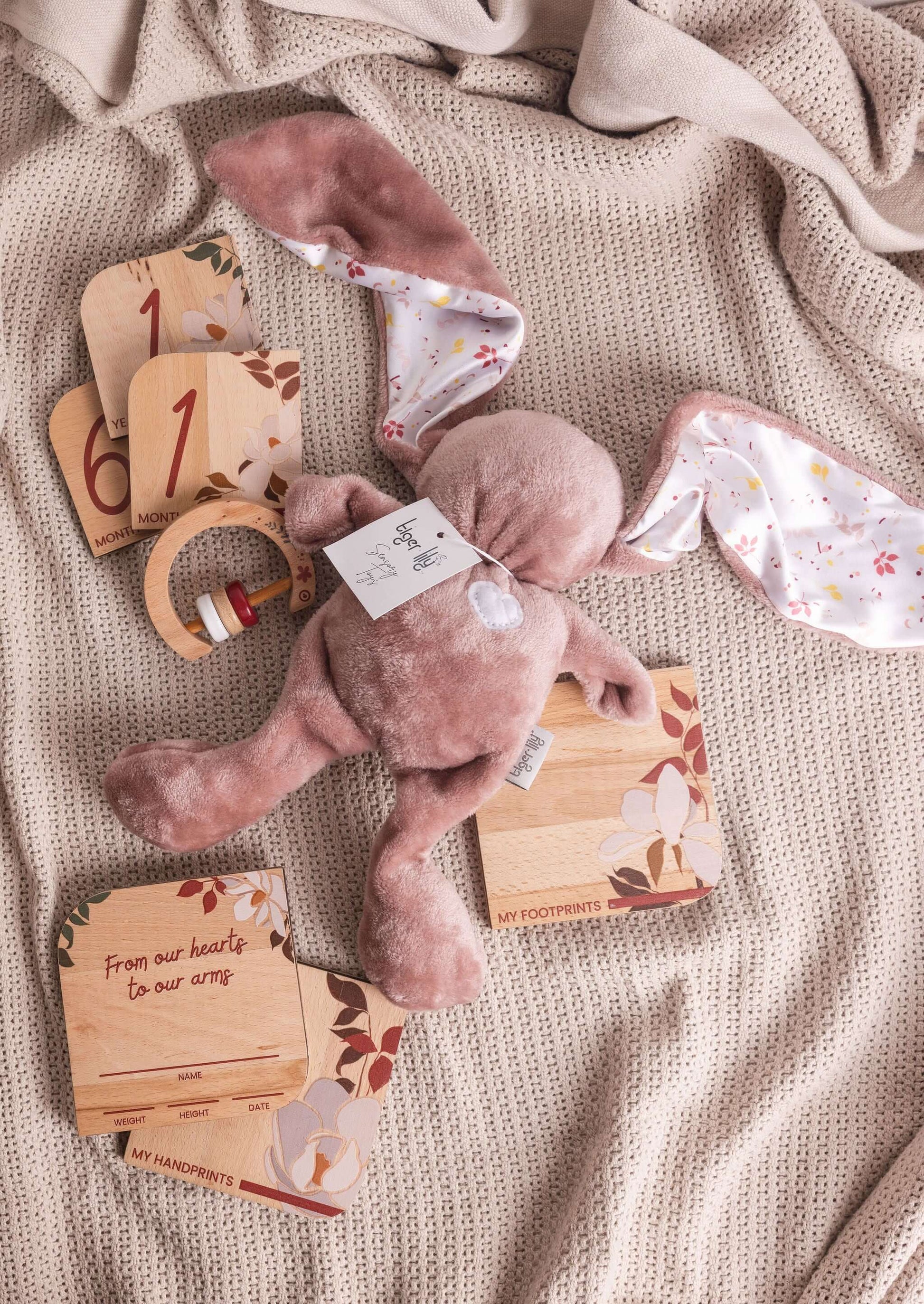 Baby gift set featuring Tiger Lily Bunny, milestone disks, and rattle on a cozy blanket.