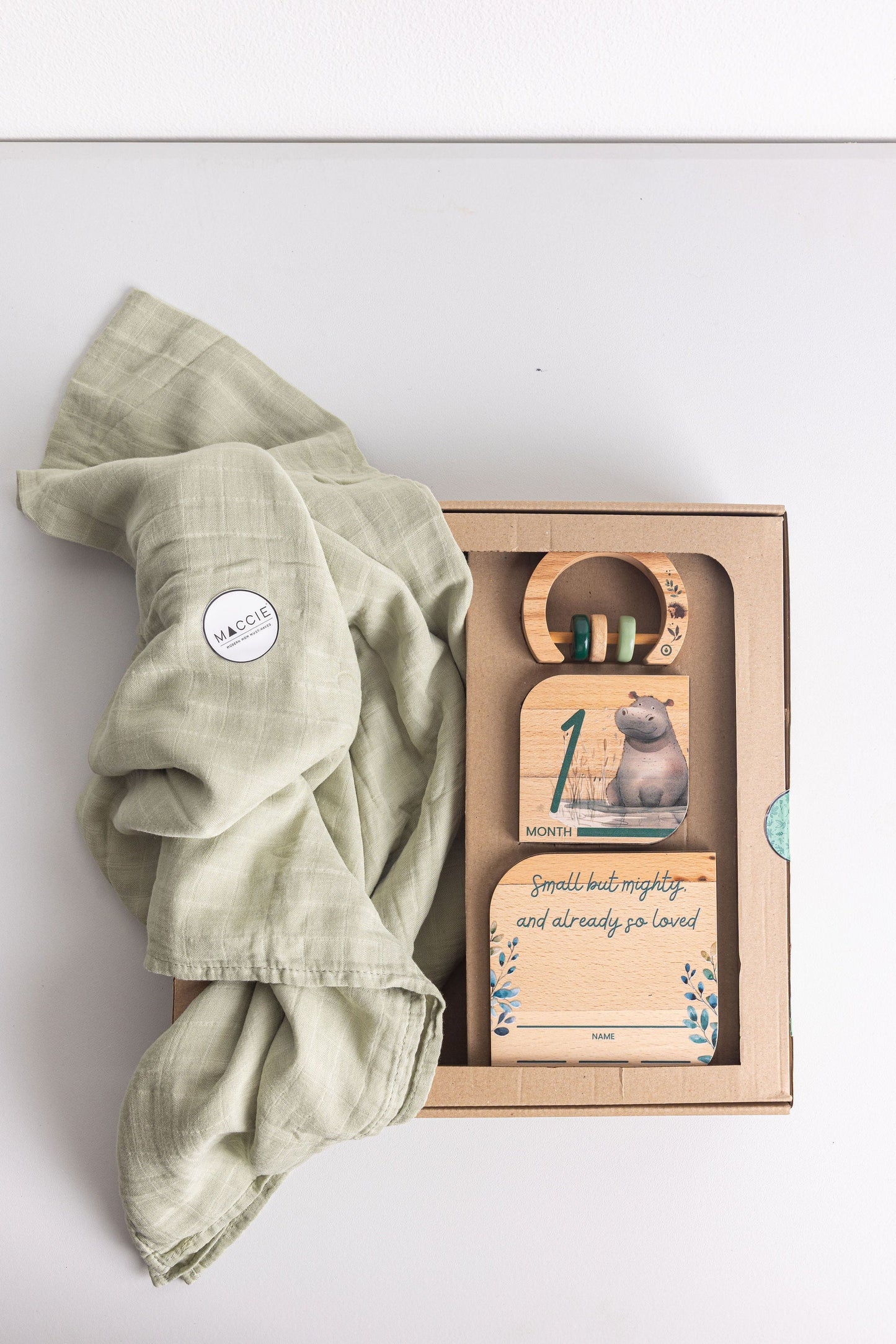 Baby Gift Set featuring Maccie Swaddle, milestone disk, and rattle on a light background.